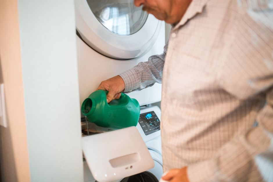 An adult man pours detergent into a washing machine for doing laundry indoors.